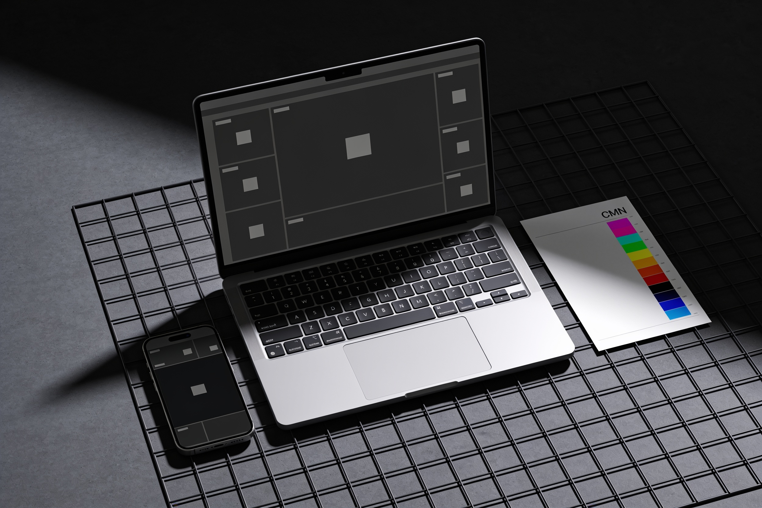 A laptop and a phone photographed top-down, both showing a blank page layout, beside a printed sheet with a colour control bar.