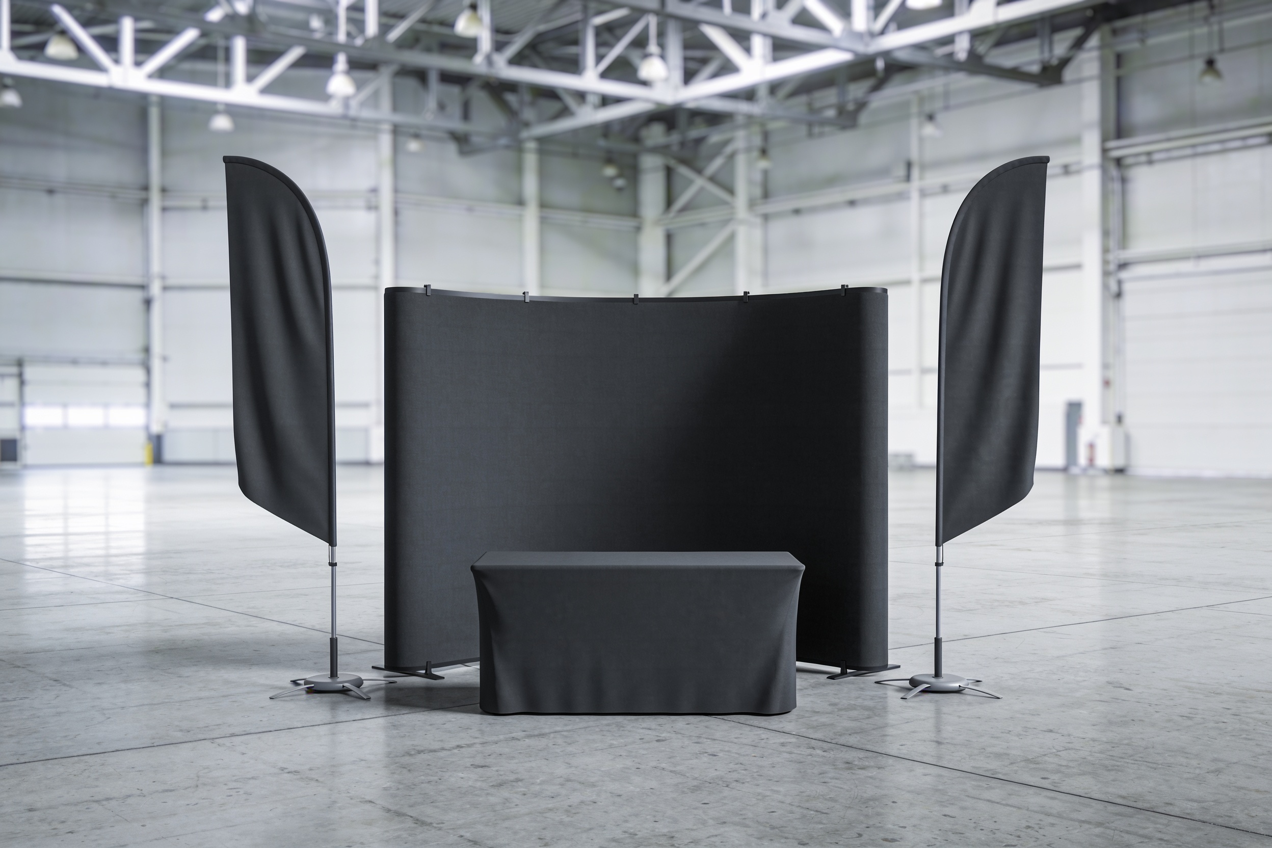A compact trade show stand in an empty hall: a fabric backdrop, a fitted table cover and two feather flags.