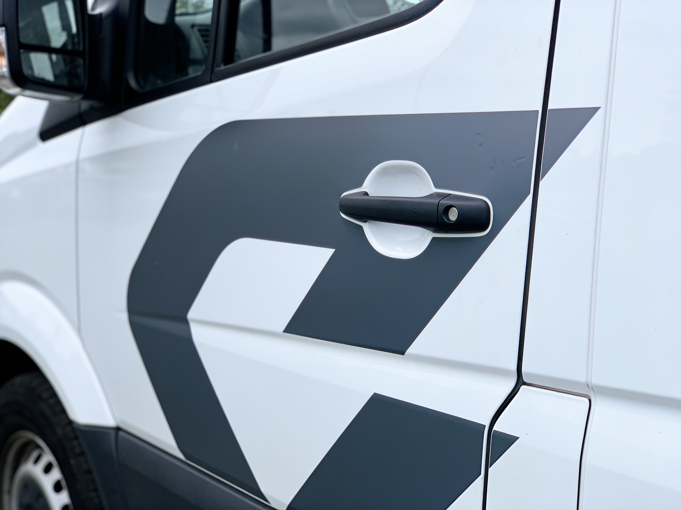 Cut vinyl on a white van door, the knife-cut edge conforming over the door seam and the handle recess.